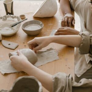 Two women engaging in pottery crafting with clay and tools on a tabletop.