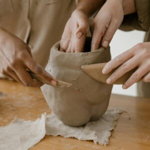 Hands shaping clay pottery collaboratively, showing craftsmanship.